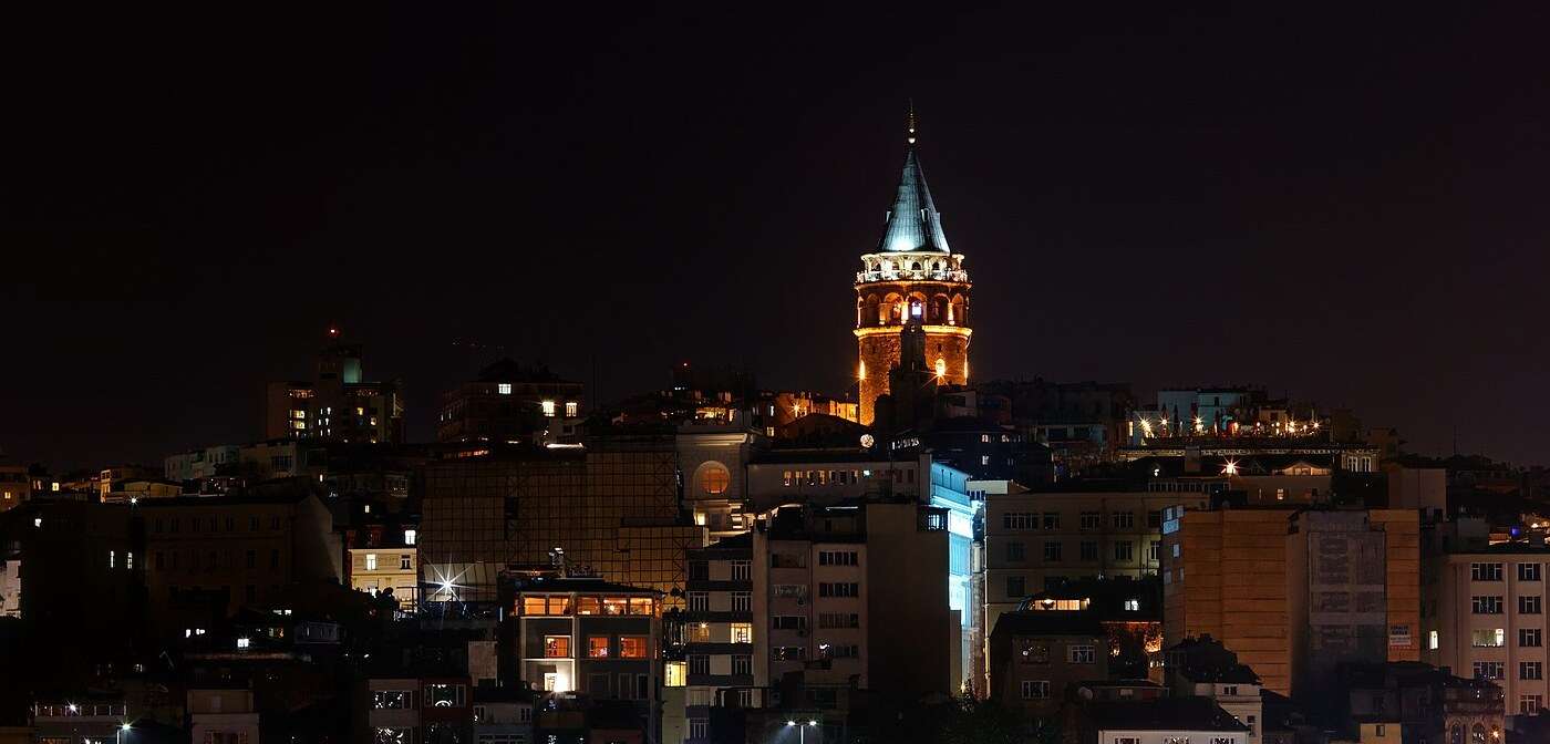 The Galata Tower lit at night above the rooftops of Beyoğlu in Istanbul